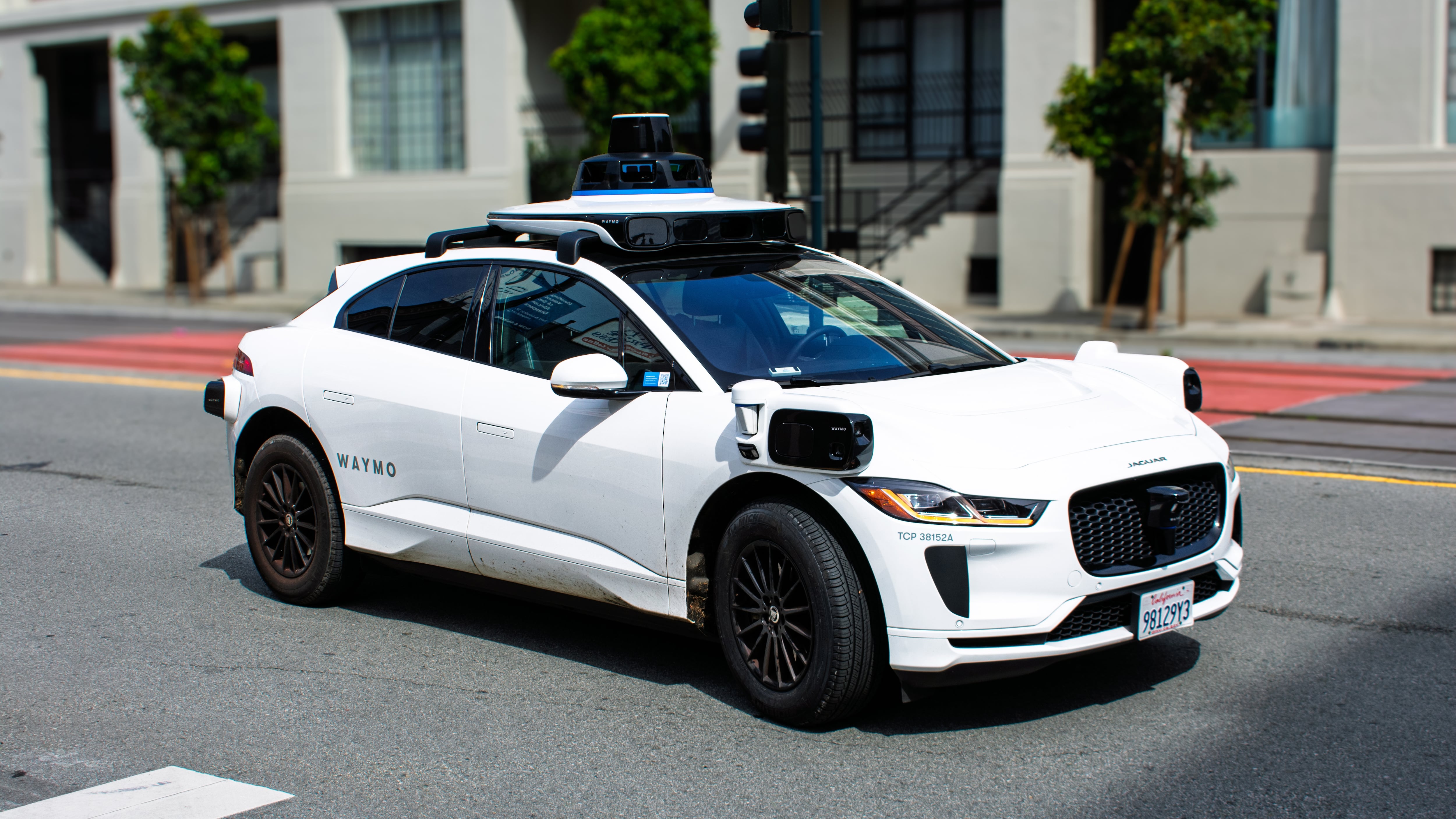 Waymo Jaguar I-PACE equipped with self-driving technology navigates a city intersection, visible sensors and cameras